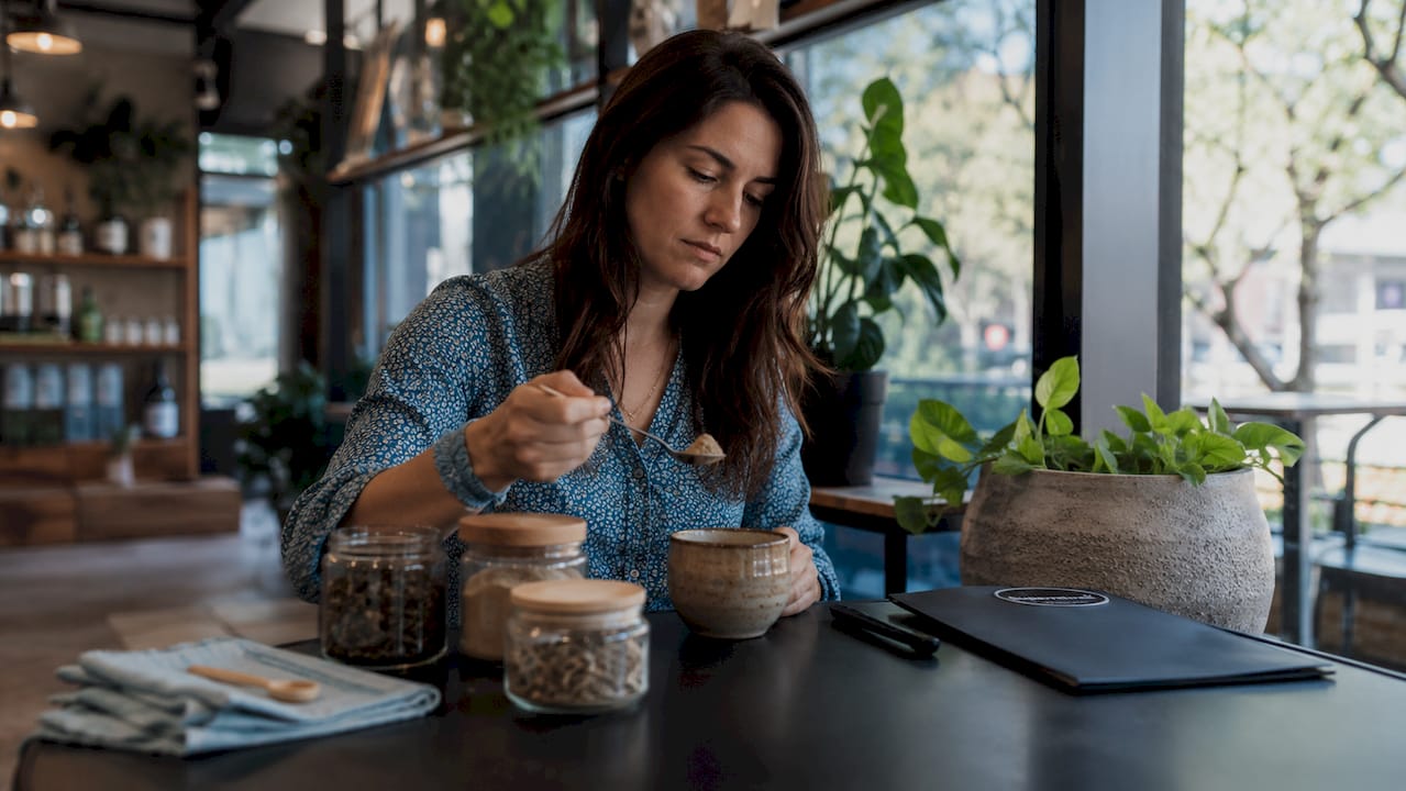 Woman preparing adaptogenic herb tea at kitchen table