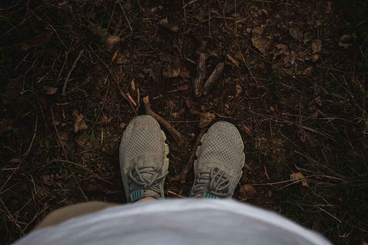 Grey sneakers on a woodland walking trail with leaves underfoot, illustrating active lifestyle movement and outdoor recovery habits