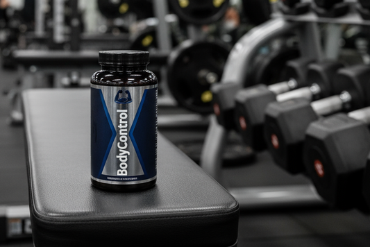 a supplement bottle that says "BodyControl" on it sitting on a workout bench next to a rack of weights